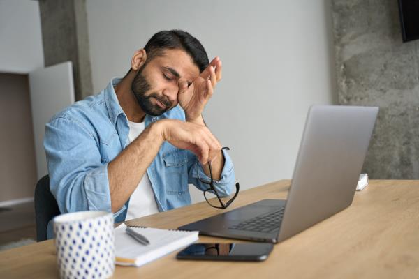 Tired man rubbing his eyes while sitting in front of a computer.