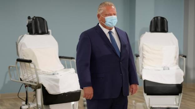 o<em></em>ntario Premier Doug Ford standing, with two medical chairs behind him. 