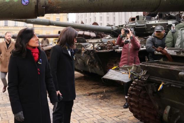 A woman in a black jacket and red scarf walks by a row of tanks