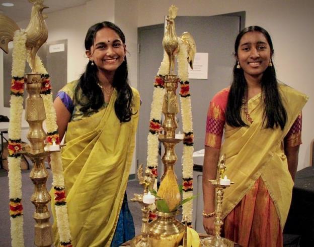 Two young girls are standing by the traditio<em></em>nal entrance for a Tamil harvest festival and heritage mo<em></em>nth celebration. They are dressed in colourful sarees.