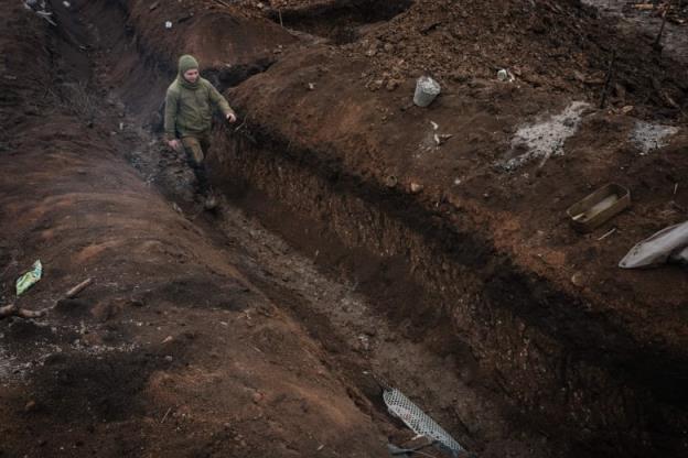 A man walks in a waist-deep trench that cuts diago<em></em>nally across the image. 